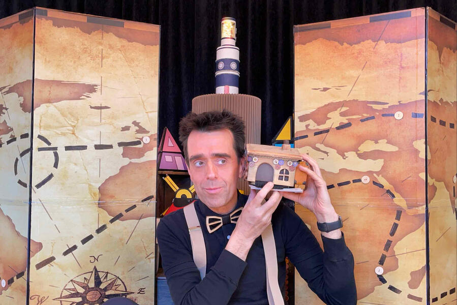 Risque-Tout Monsieur Fred qui tient Risque-Tout devant le village et une carte géante du monde.