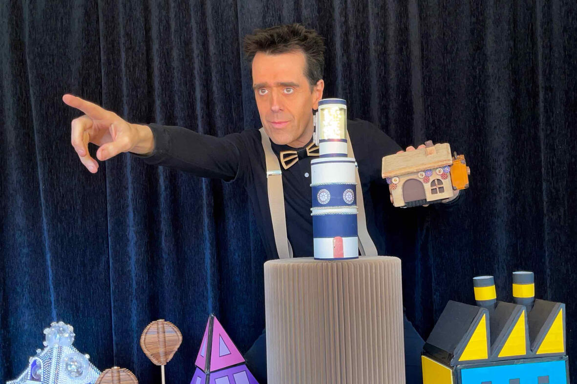 Photo du spectacle “Risque-Tout” : Monsieur Fred anime la scène avec la petite maison, l’île et le personnage principal devant un public d’enfants.